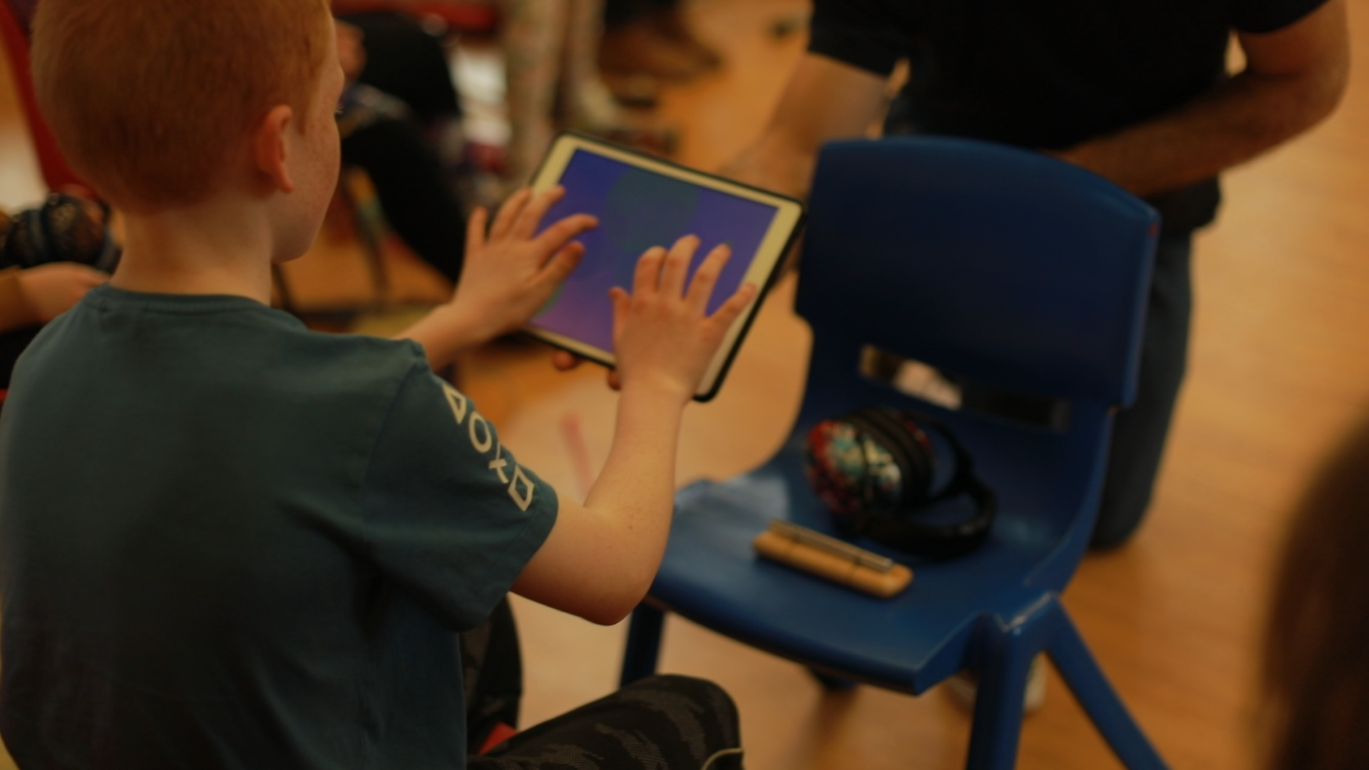 A boy with ginger hair playing an iPad, viewed from the back